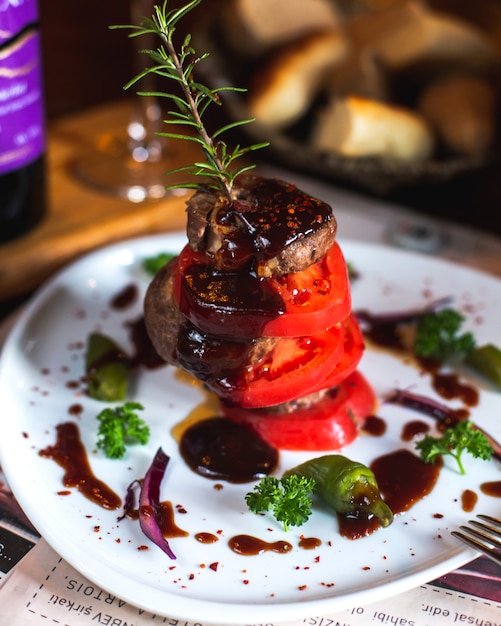 Carne frita com fatias de tomate, verduras, molho e raminho de alecrim