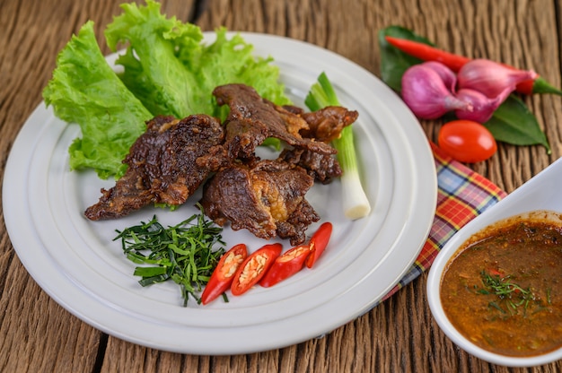 Carne frita comida tailandesa em um prato branco com cebolinha, folhas de limão kaffir, pimentões, salada, cebola roxa e tomate.