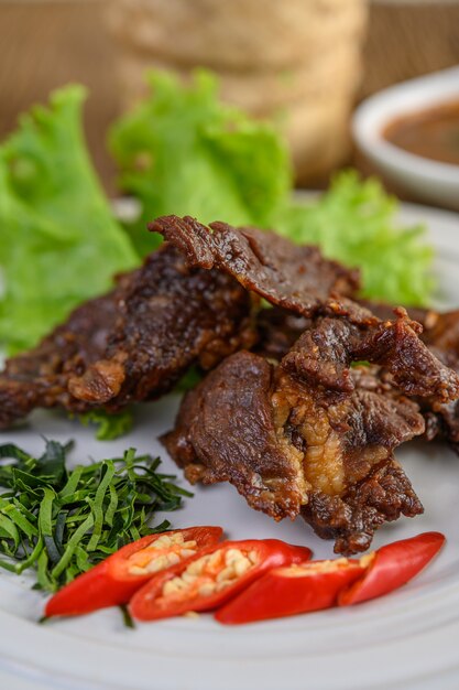 Carne frita comida tailandesa em um prato branco com cebolinha, folhas de limão kaffir, pimentões, salada e pasta de pimentão em um copo.