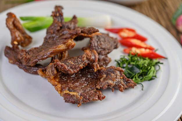 Carne frita comida tailandesa em um prato branco com cebolinha, folhas de limão kaffir, pimentões, salada e pasta de pimentão em um copo.