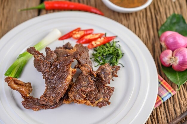 Carne frito comida tailandesa em um prato branco com cebolinha, folhas de limão kaffir, pimentões, cebolas vermelhas e tomates.