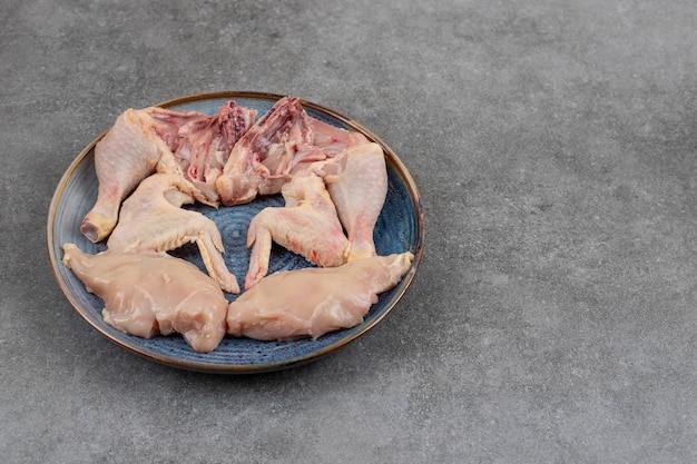 Carnes frescas de frango orgânico no prato azul sobre a mesa cinza.