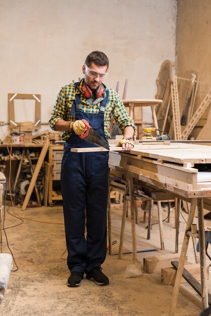 Carpinteiro masculino cortando a prancha de madeira com serrote