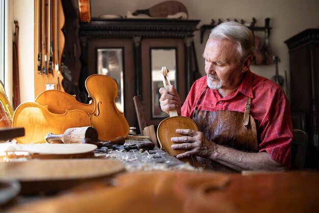 Carpinteiro sênior montando peças de instrumento de violino em sua oficina de carpinteiro