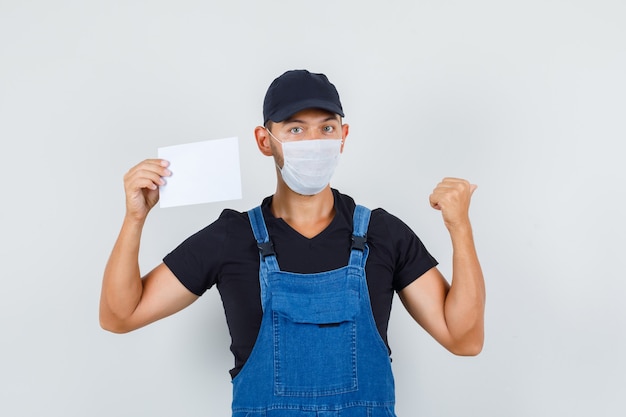 Carregador jovem de uniforme, máscara segurando a folha de papel enquanto aponta para trás, vista frontal.