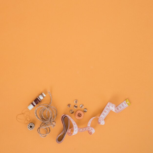 Carretel marrom; corda; botões e fita métrica em um pano de fundo laranja