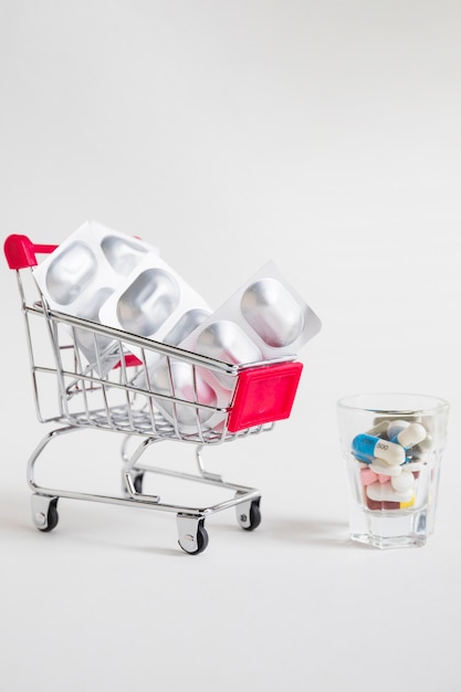 Carrinho de compras com bolha do comprimido e medicamentos em vidro no fundo branco