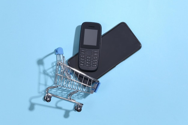 Carrinho de compras com botão de telefone e smartphone moderno sobre fundo azul. vista do topo Foto Premium