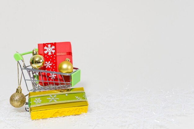 Carrinho de compras com caixas de presente e esferas douradas em um floco de neve em um fundo branco