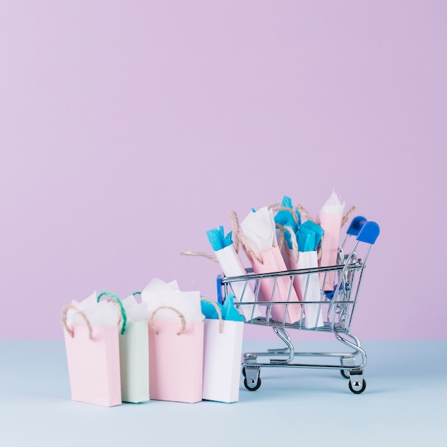 Carrinho em miniatura, cheio de sacolas de papel na frente de fundo rosa