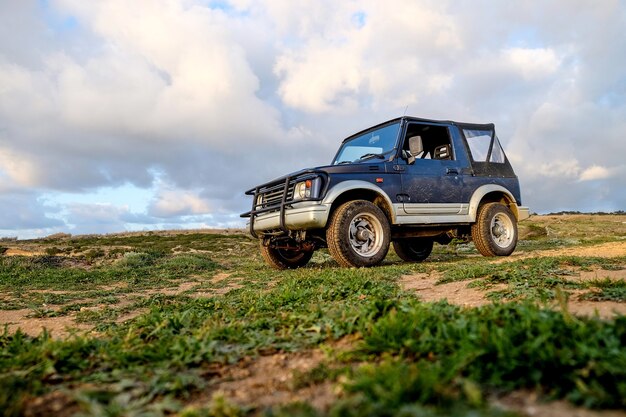 Carro azul na colina coberto pela grama sob a luz do sol e um céu nublado