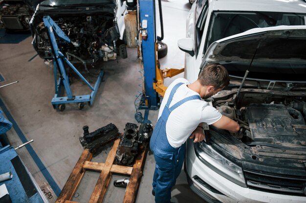 Carro branco de luxo. Funcionário com uniforme azul trabalha no salão automóvel