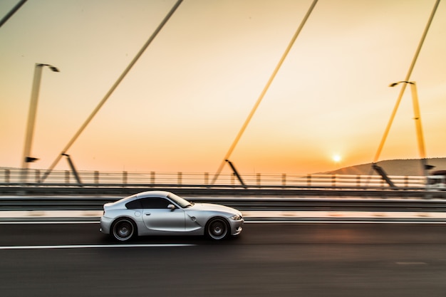 Foto grátis carro desportivo de cor metálica na ponte por do sol.