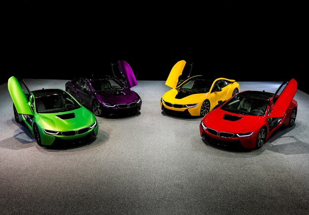 Carros esporte sedan verde, amarelo, vermelho, roxo e violeta em pé no espaço escuro