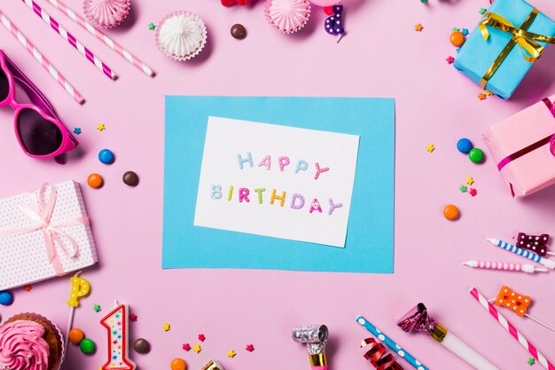 Cartão de feliz aniversário rodeado com itens de aniversário no pano de fundo rosa