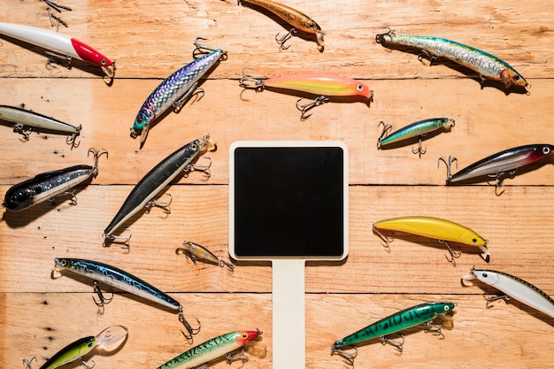 Cartaz preto em branco cercado com iscas de pesca coloridos na mesa de madeira