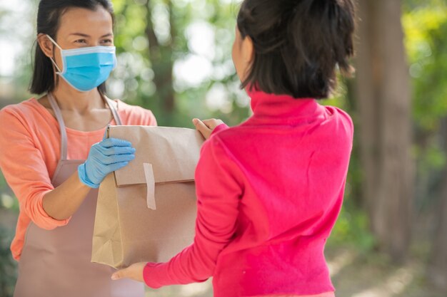 Carteiro, entregador usando máscara carrega uma pequena caixa para entregar ao cliente na frente da porta de casa. mulher usando máscara prevenir covid 19, surto de infecção por coronavírus. conceito de compras de entrega em domicílio.