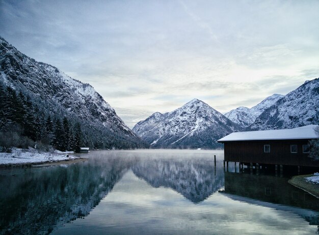 Casa residencial perto do lago cercada por belas montanhas rochosas cobertas de neve