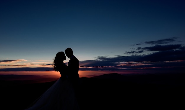 Casal abraça antes do céu violeta sobre as montanhas
