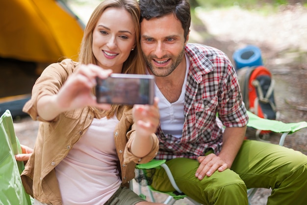 Casal acampando na floresta e tirando uma foto