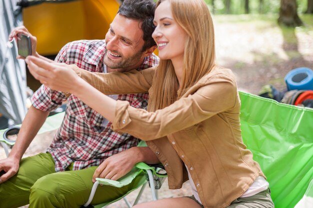 Casal acampando na floresta e tirando uma foto