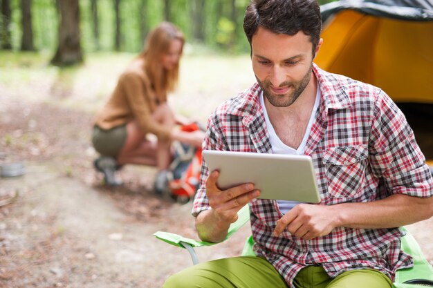 Casal acampando na floresta. Homem usando um tablet digital