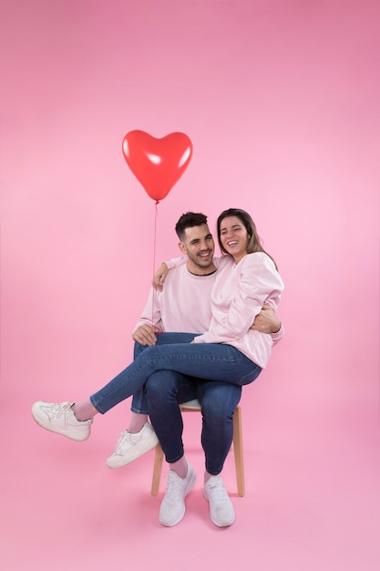 Foto grátis casal alegre com balão de coração abraçando na cadeira