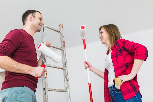 Foto grátis casal alegre com rolos de pintura e escada
