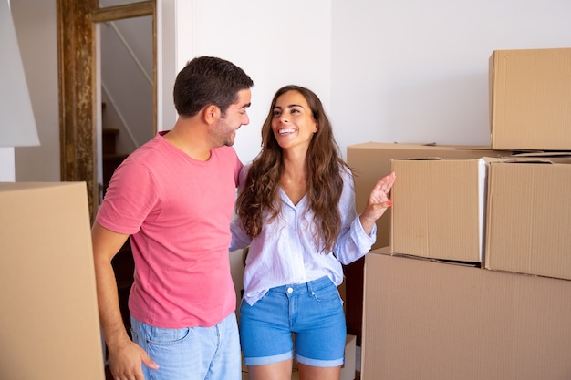 Casal alegre da família parado entre caixas de papelão, se abraçando e discutindo sobre seu novo apartamento