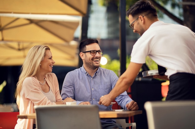 Casal alegre desfrutando em um café enquanto o garçom está servindo seu pedido na mesa