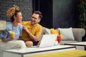 Foto grátis casal alegre rindo enquanto fala sobre algo engraçado e usando laptop em um café
