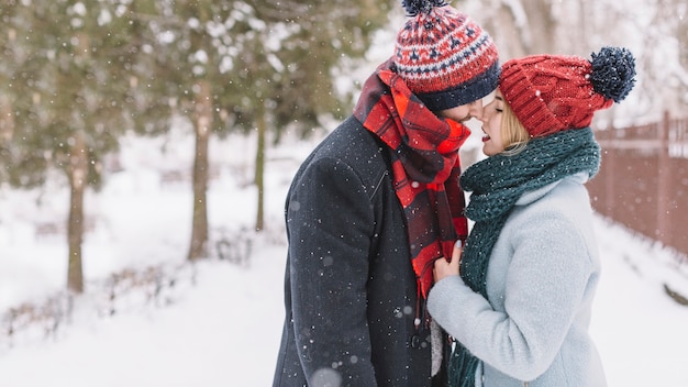 Casal amável na moda se beija na queda de neve