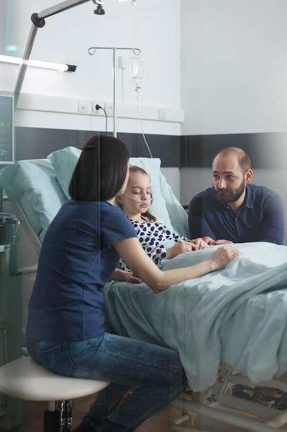 Casal ansioso e estressado discutindo sobre a evolução da doença da menina enquanto na sala de recuperação de pacientes pediátricos do hospital. Pais jovens nervosos preocupados falando sobre tratamento de saúde.