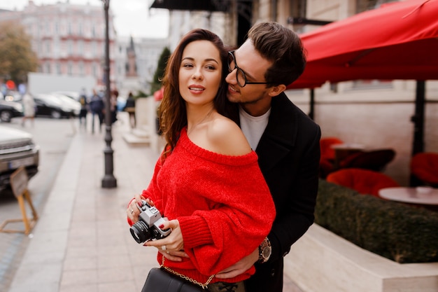 Casal apaixonado, constrangedor e posando na rua de férias. Humor romântico. Linda mulher morena segurando a câmera de filme.