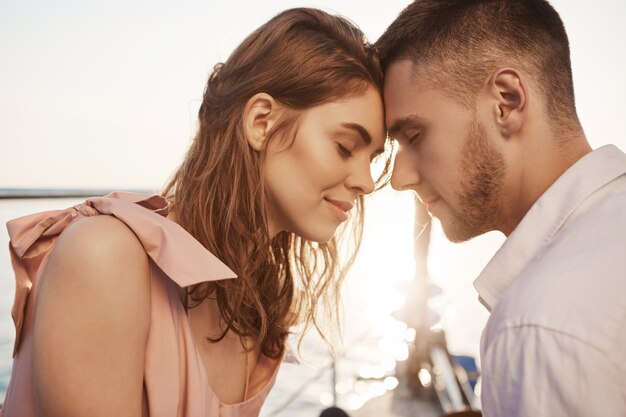 casal apaixonado, fechando os olhos e tocando com a testa enquanto navegava no iate, tendo férias. Namorado romântico arranjado data no mar para apreciar o pôr do sol com a namorada