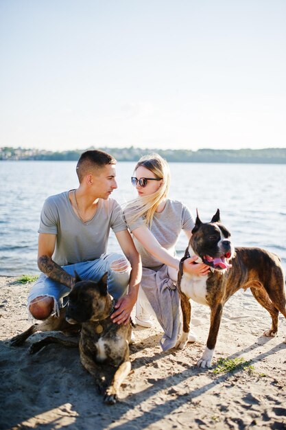 Casal apaixonado por dois cães pit bull terrier contra o lado da praia