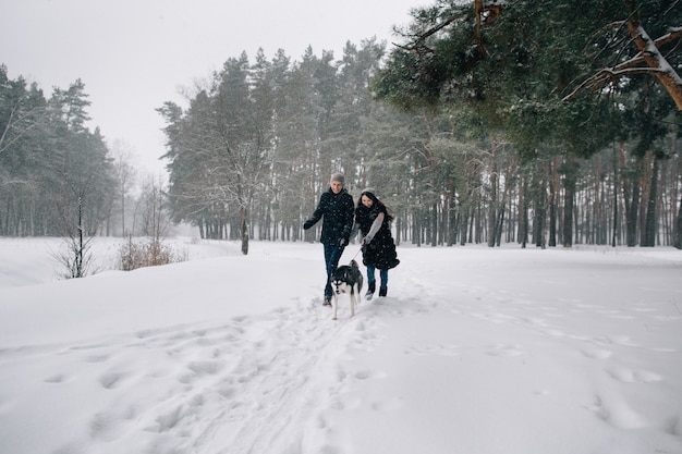 Casal apaixonado se divertir com o cão Husky no dia frio de inverno nevado