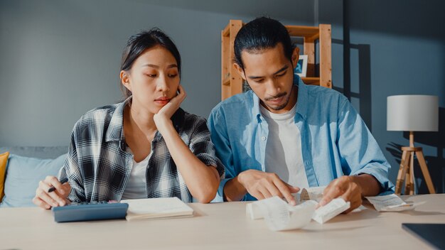 Casal asiático estressado, homem e mulher, usam calculadora para calcular o orçamento familiar