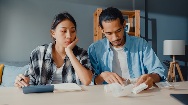 Casal asiático estressado, homem e mulher, usam calculadora para calcular o orçamento familiar