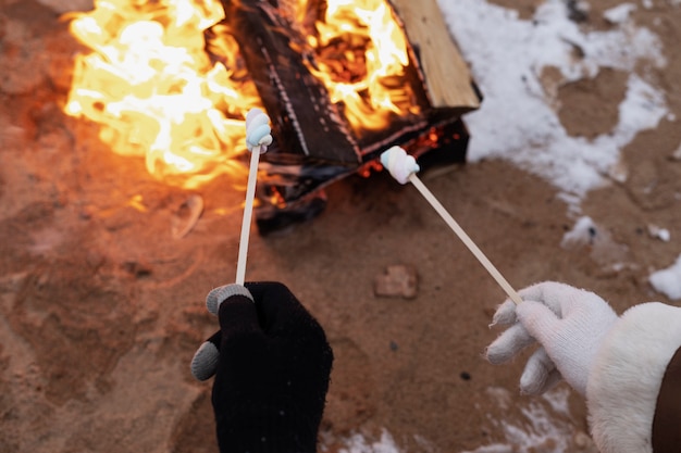 Casal assando marshmallows no fogo durante uma viagem de inverno na praia