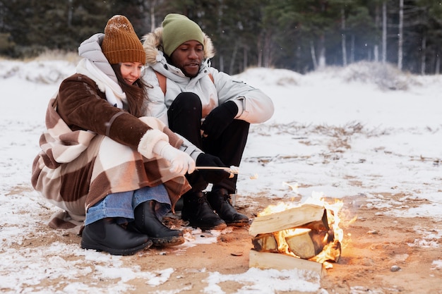 Casal assando marshmallows no fogo durante uma viagem de inverno na praia