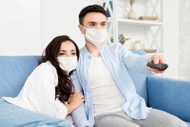 Casal assistindo tv em casa com máscaras faciais