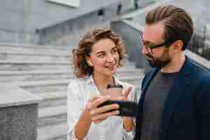 Foto grátis casal atraente de homem e mulher conversando no centro urbano da cidade, segurando o telefone e olhando