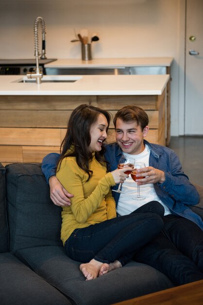 Casal bebendo vinho tinto sentado no sofá da sala