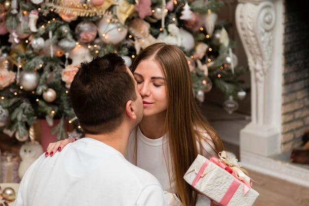 Foto grátis casal beijando com presente na frente da árvore de natal