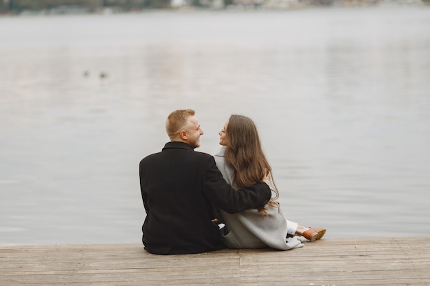 Casal bonito em um parque. Senhora com um casaco cinza. Pessoas no cais.