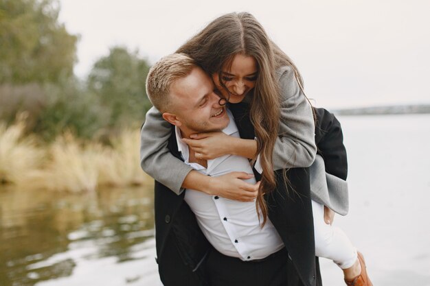 Casal bonito em um parque. Senhora com um casaco cinza. Pessoas no cais.