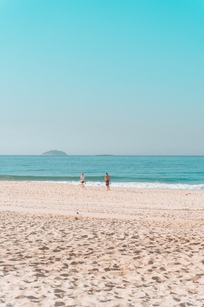 Casal caminhando ao longo da costa em uma praia ensolarada com um céu sem nuvens acima