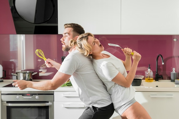 Casal cantando dentro de casa na cozinha, sentado de lado