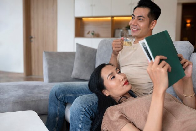 Casal carinhoso em casa no sofá lendo livro e tomando uma bebida